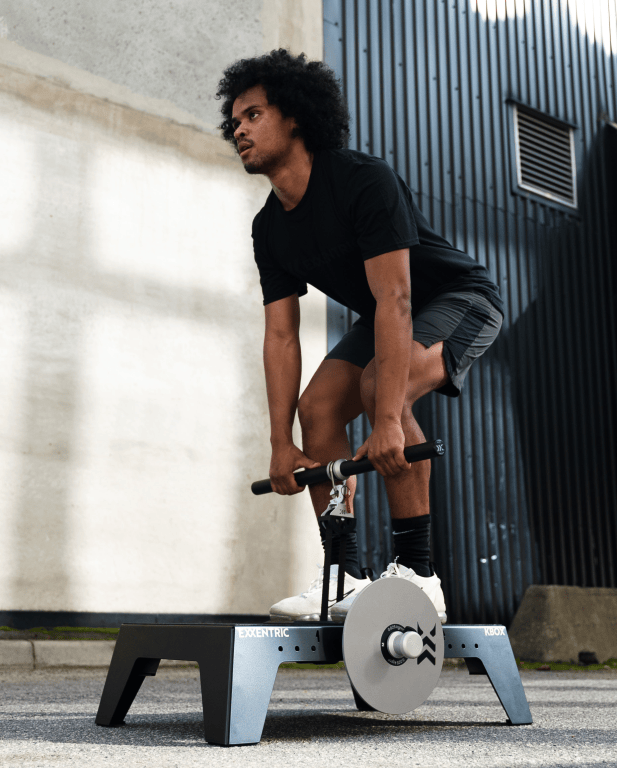 Ein Mann mit lockigem Haar führt eine Übung an einer Trainingsstation durch, die mit einer Hantel ausgestattet ist.