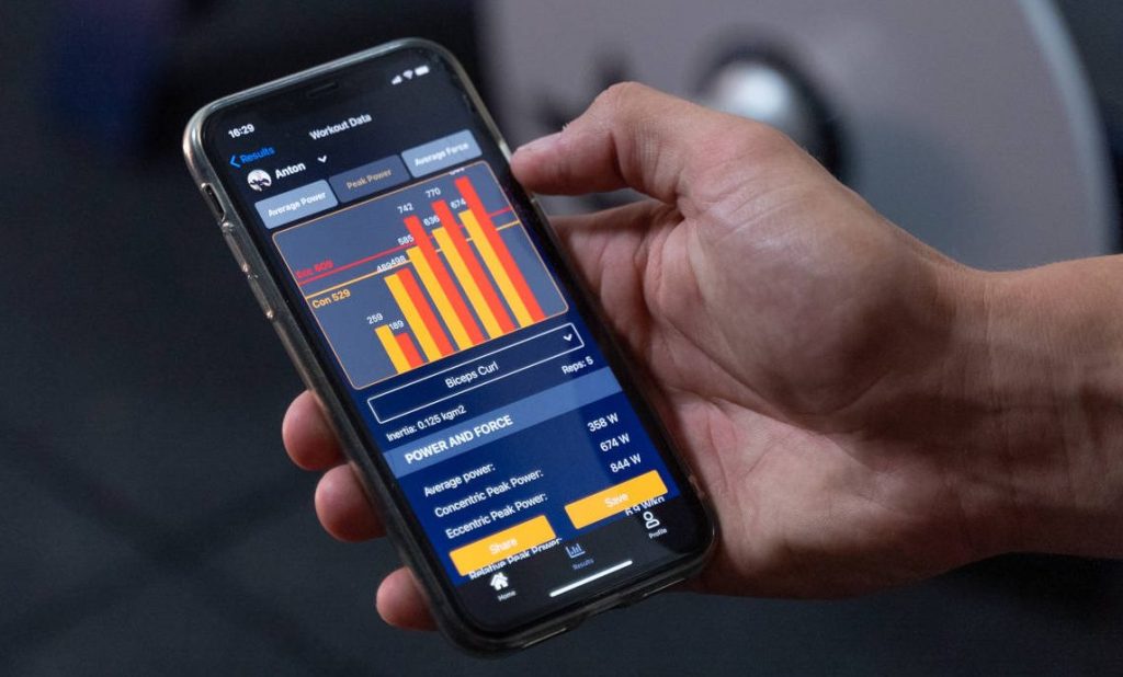 Ein Benutzer hält ein Smartphone, auf dem eine Fitnessapp mit Workout-Daten und Leistungsstatistiken angezeigt wird.